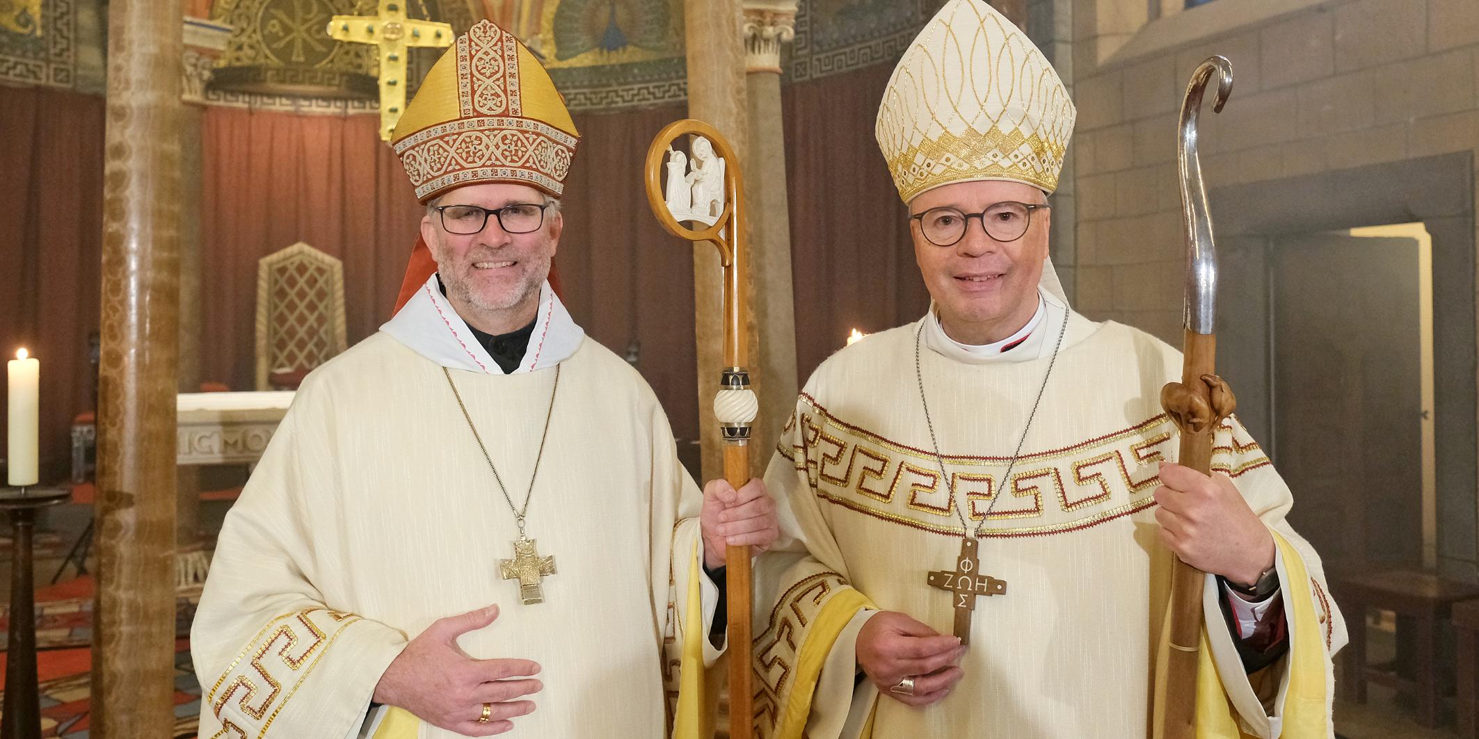 Zwei Männer mit Bischofsmützen schauen lächelnd in die Kamera