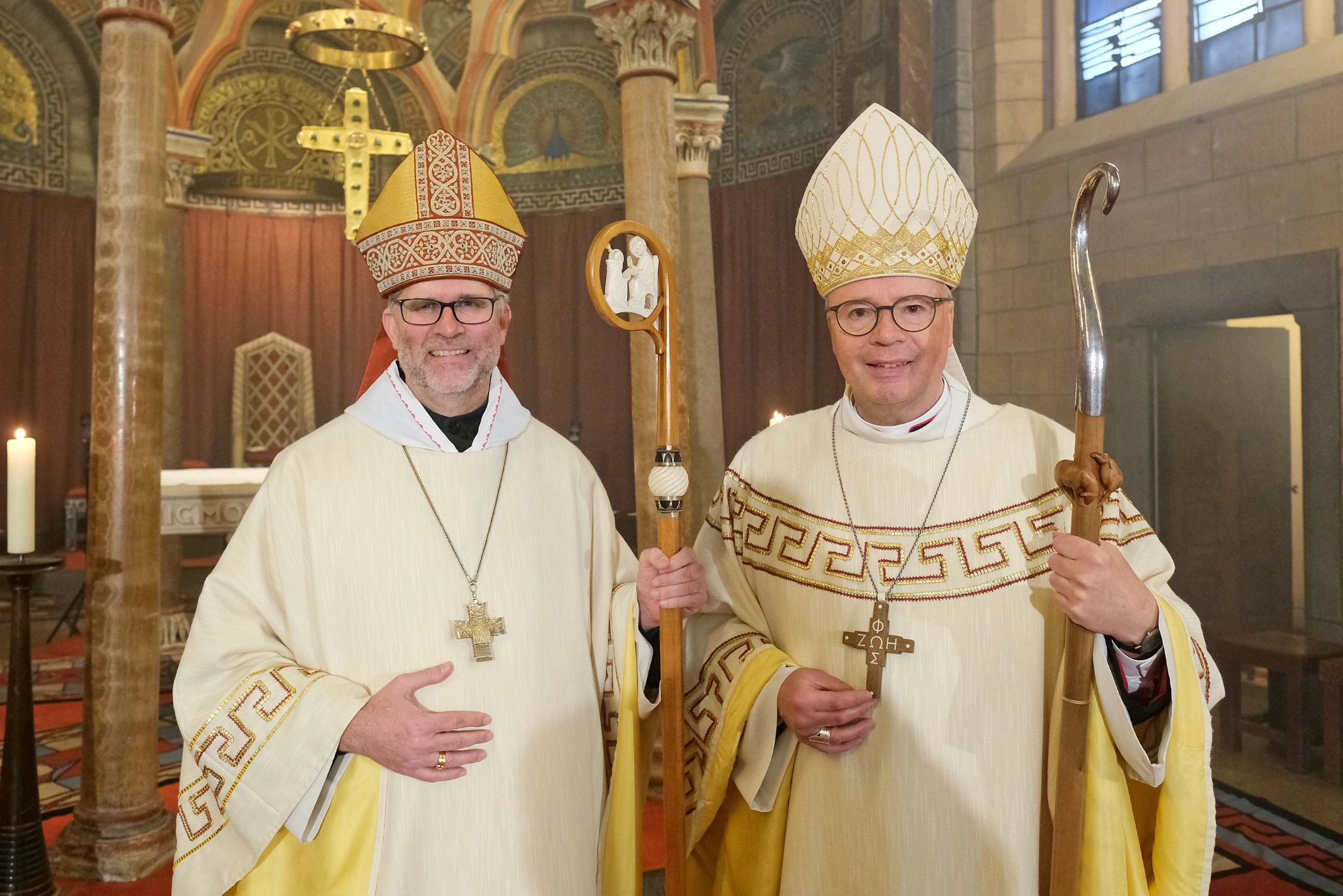 Zwei Männer mit Bischofsmützen schauen lächelnd in die Kamera