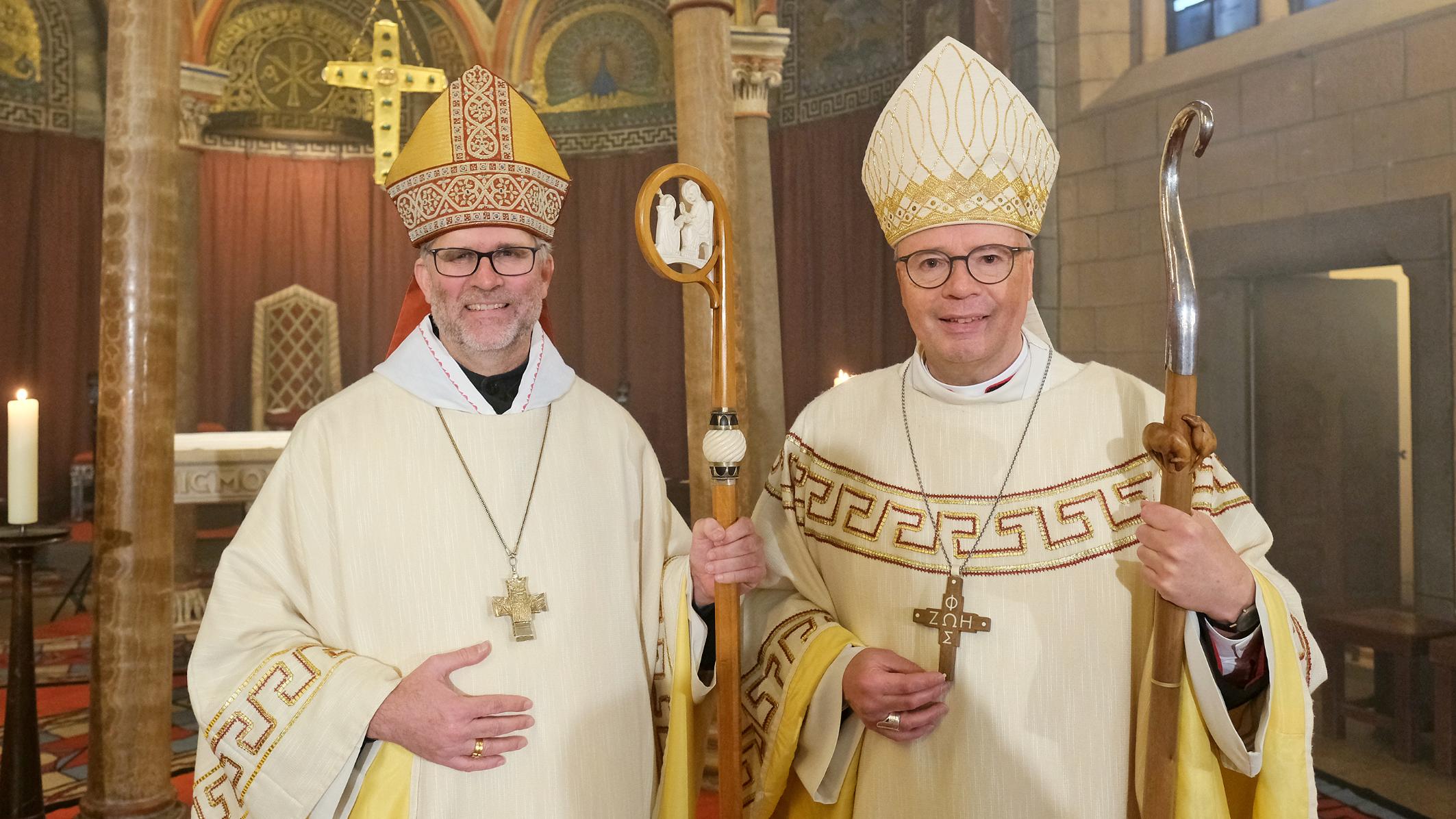 Zwei Männer mit Bischofsmützen schauen lächelnd in die Kamera