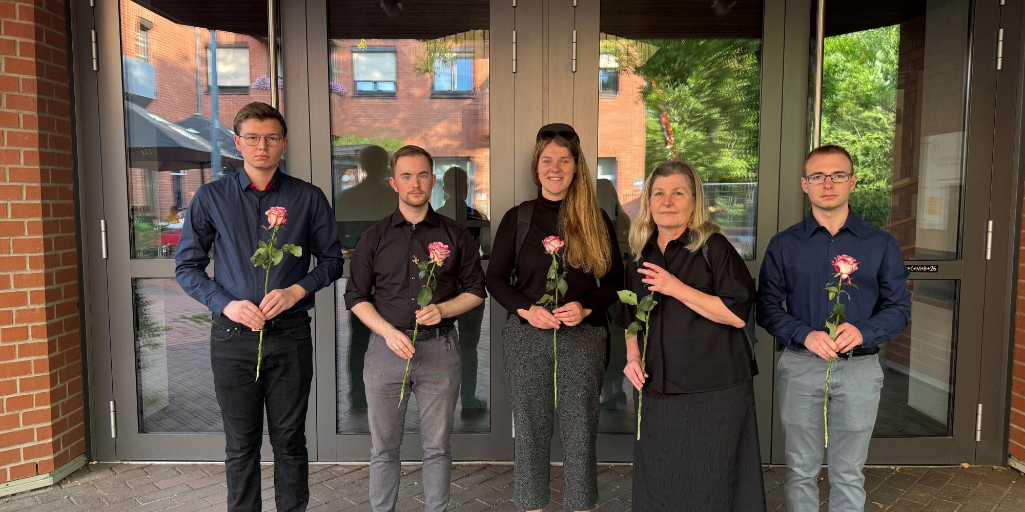 Dunkel gekleidete Menschen blicken in die Kamera und halten Rosen in den Händen (c) Kathrin Schmitt Dunkel gekleidete Menschen blicken in die Kamera und halten Rosen in den Händen