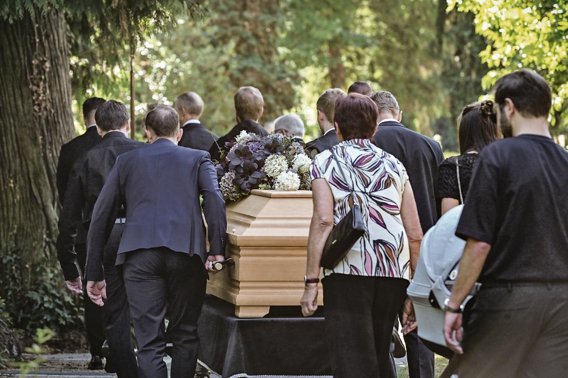 Trauernde folgen Sargträgern zum Grab.
