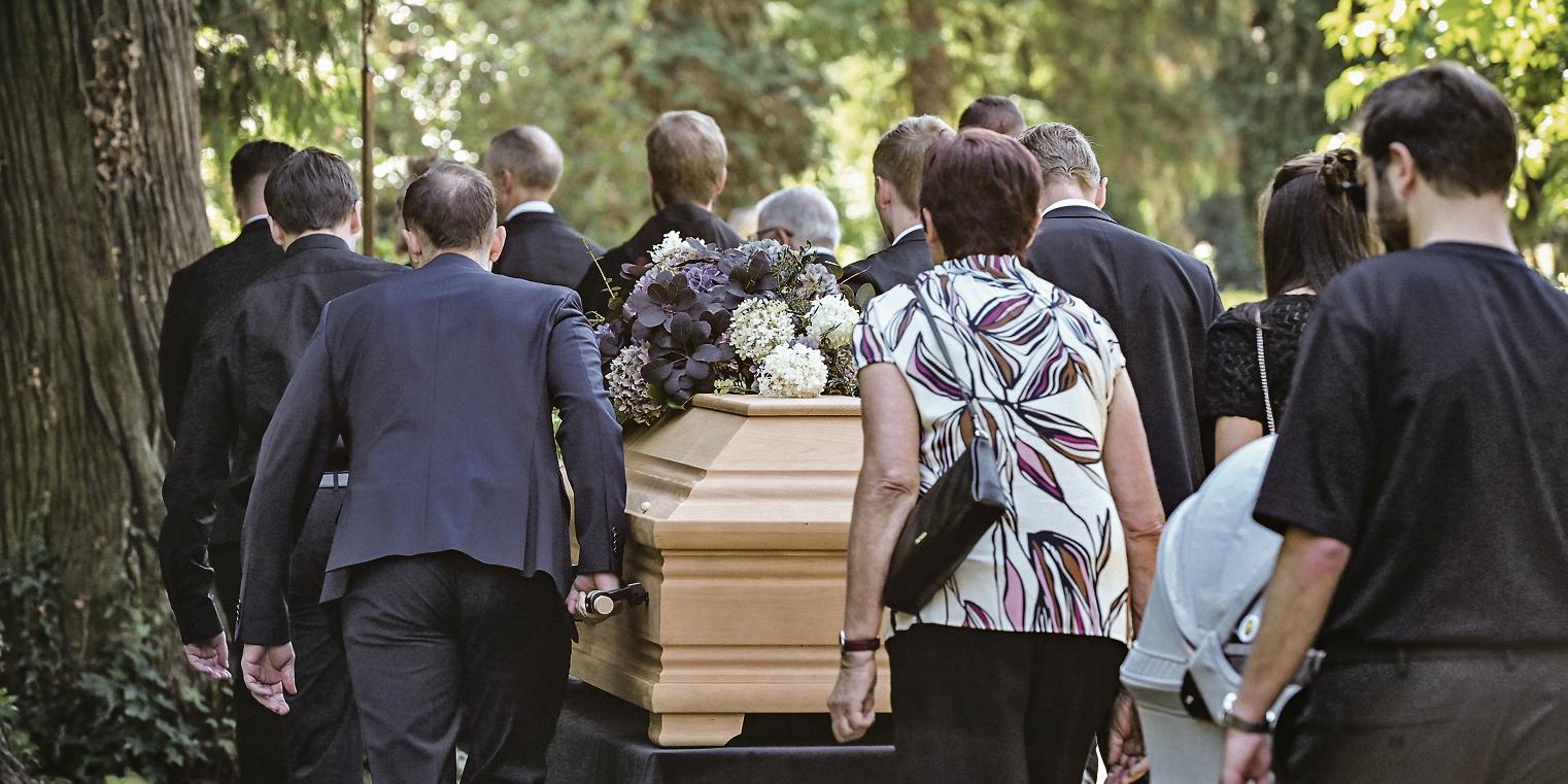 Trauernde folgen Sargträgern zum Grab.
