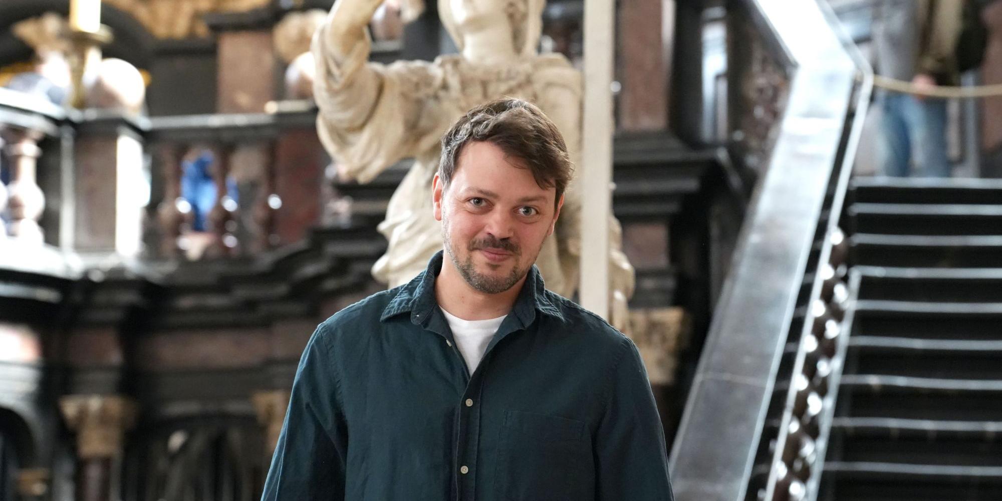 Schauspieler Benjamin Kelm im Dom. Hinter ihm die Figur der heiligen Helena, der er unter anderem seine Stimme leiht.