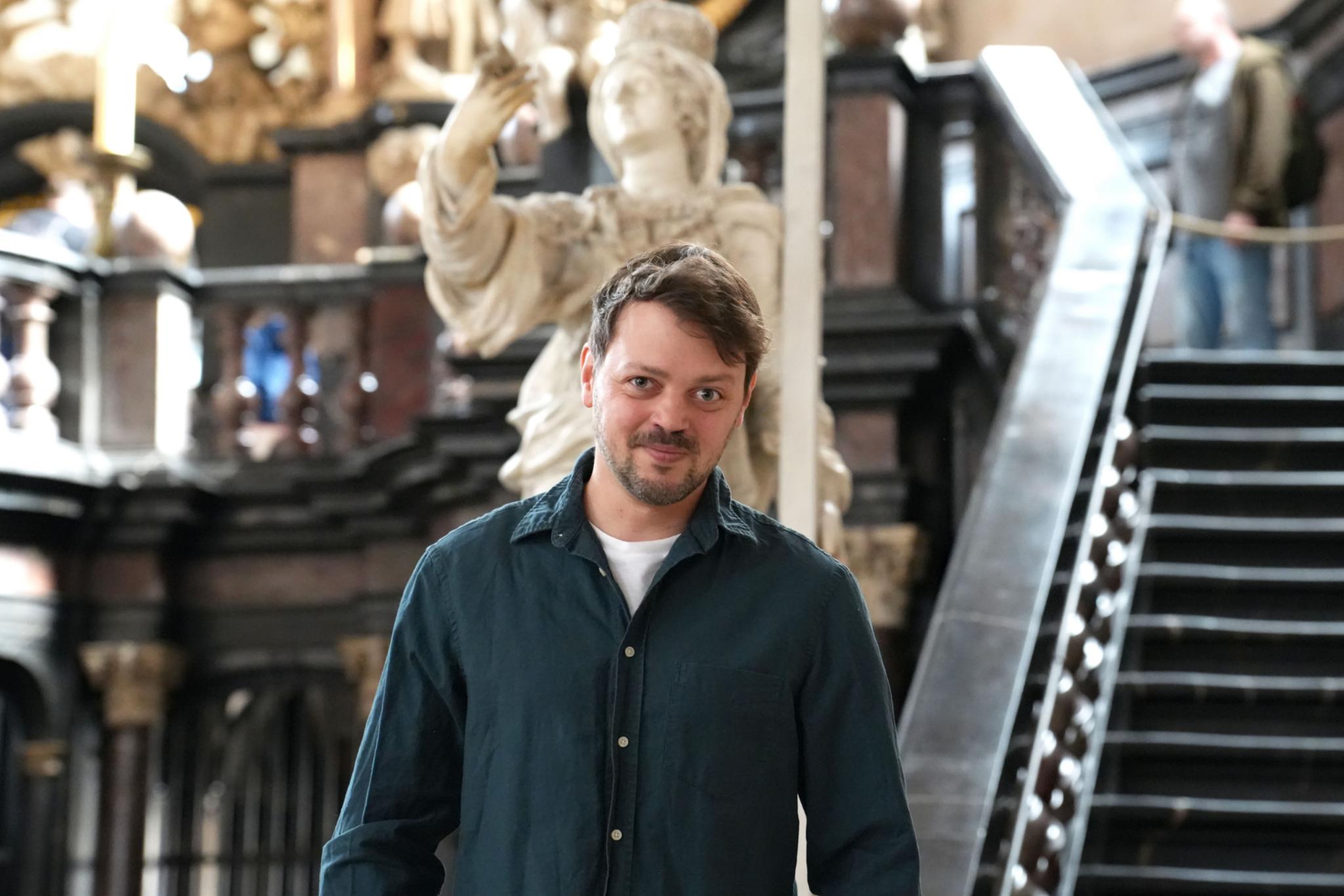 Schauspieler Benjamin Kelm im Dom. Hinter ihm die Figur der heiligen Helena, der er unter anderem seine Stimme leiht.