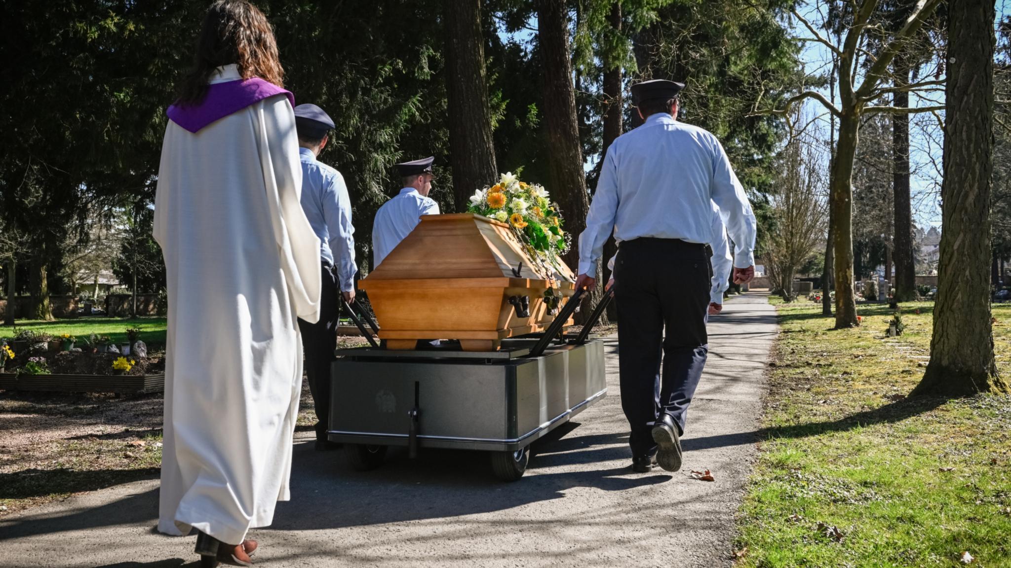 Eine Frau in liturgischem Gewand geht hinter einem Sarg her