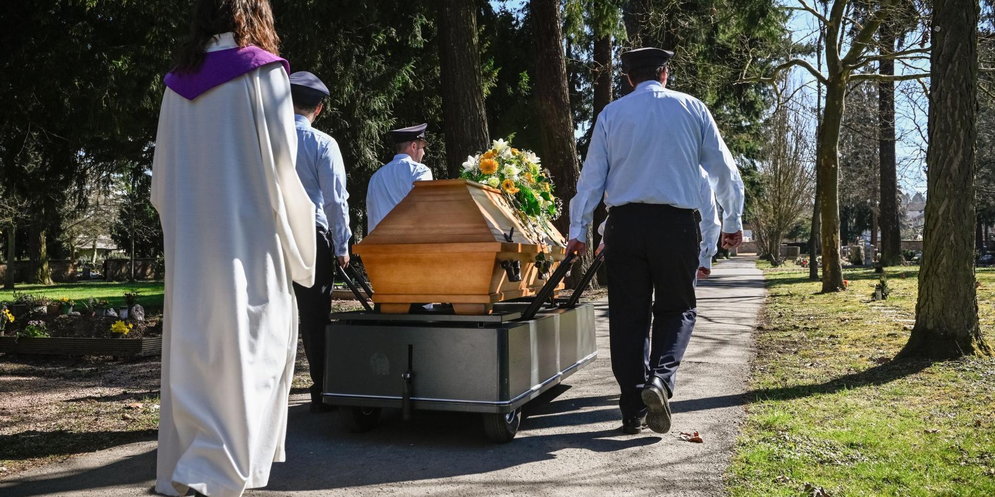 Eine Frau in liturgischem Gewand geht hinter einem Sarg her