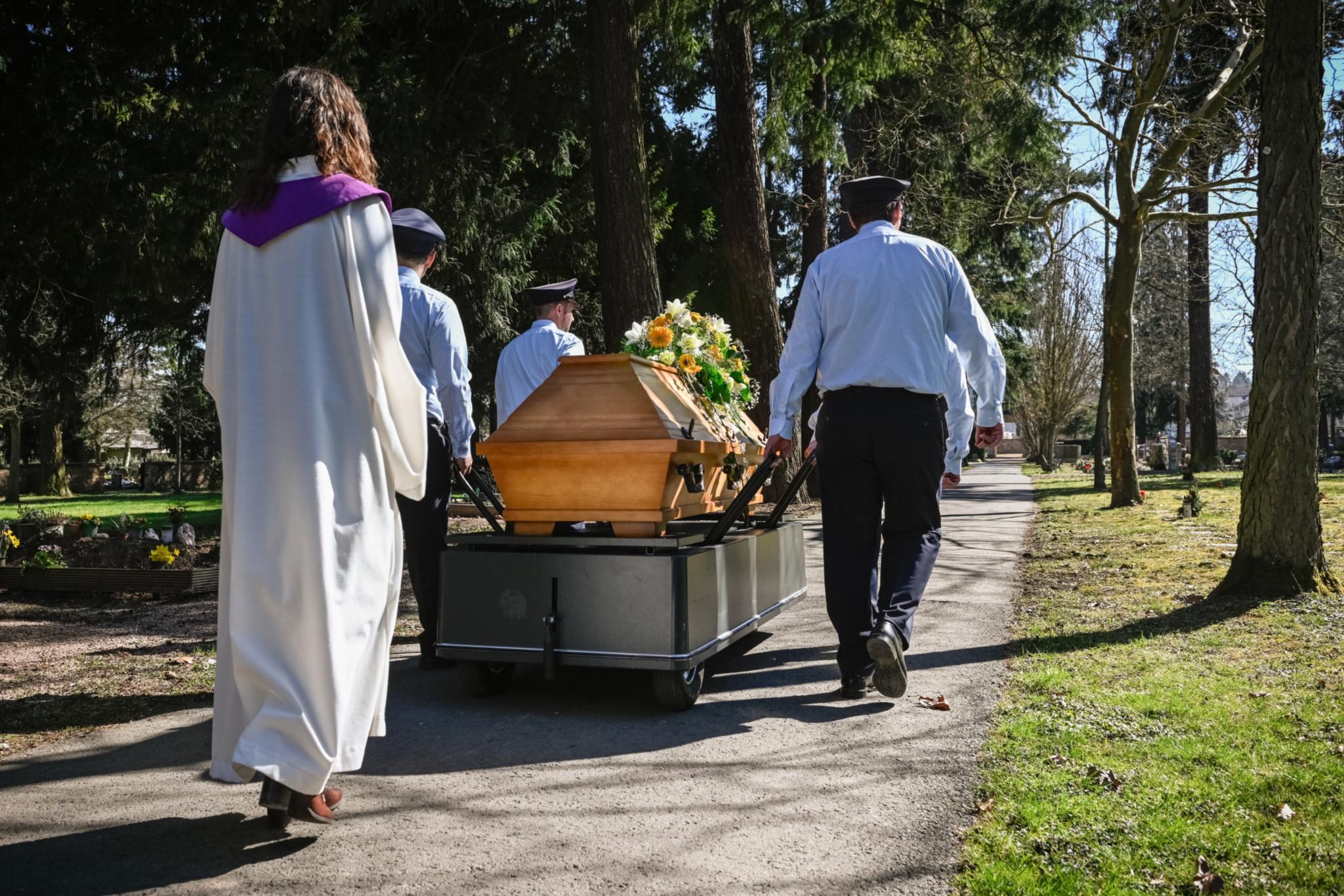Eine Frau in liturgischem Gewand geht hinter einem Sarg her