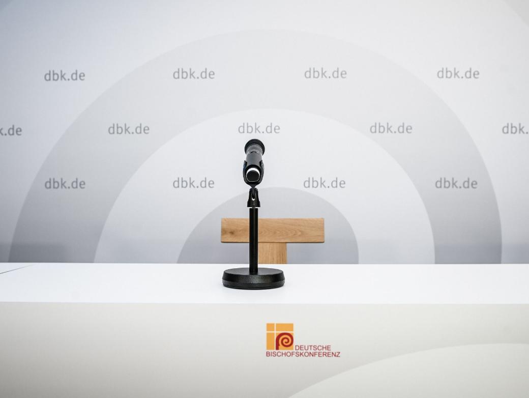 Ein Mikrofon vor einem leeren Stuhl, hinten eine Wand mit DBK-Logo