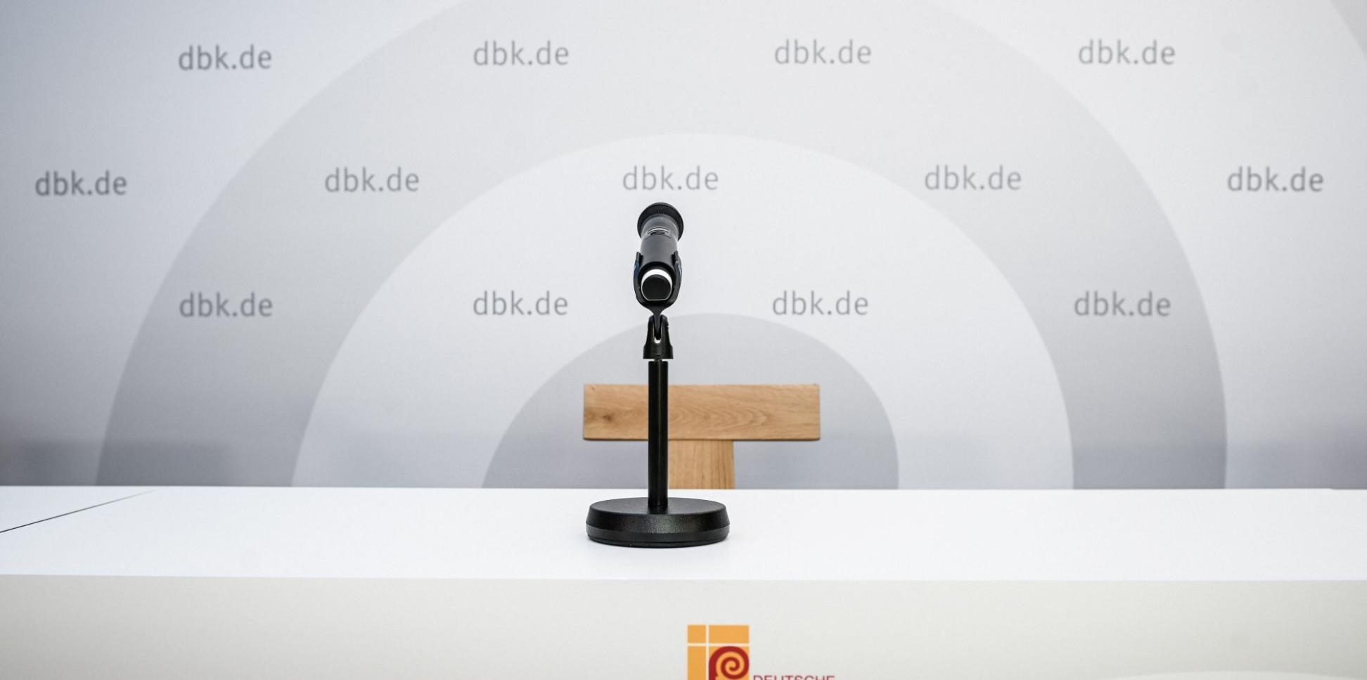 Ein Mikrofon vor einem leeren Stuhl, hinten eine Wand mit DBK-Logo
