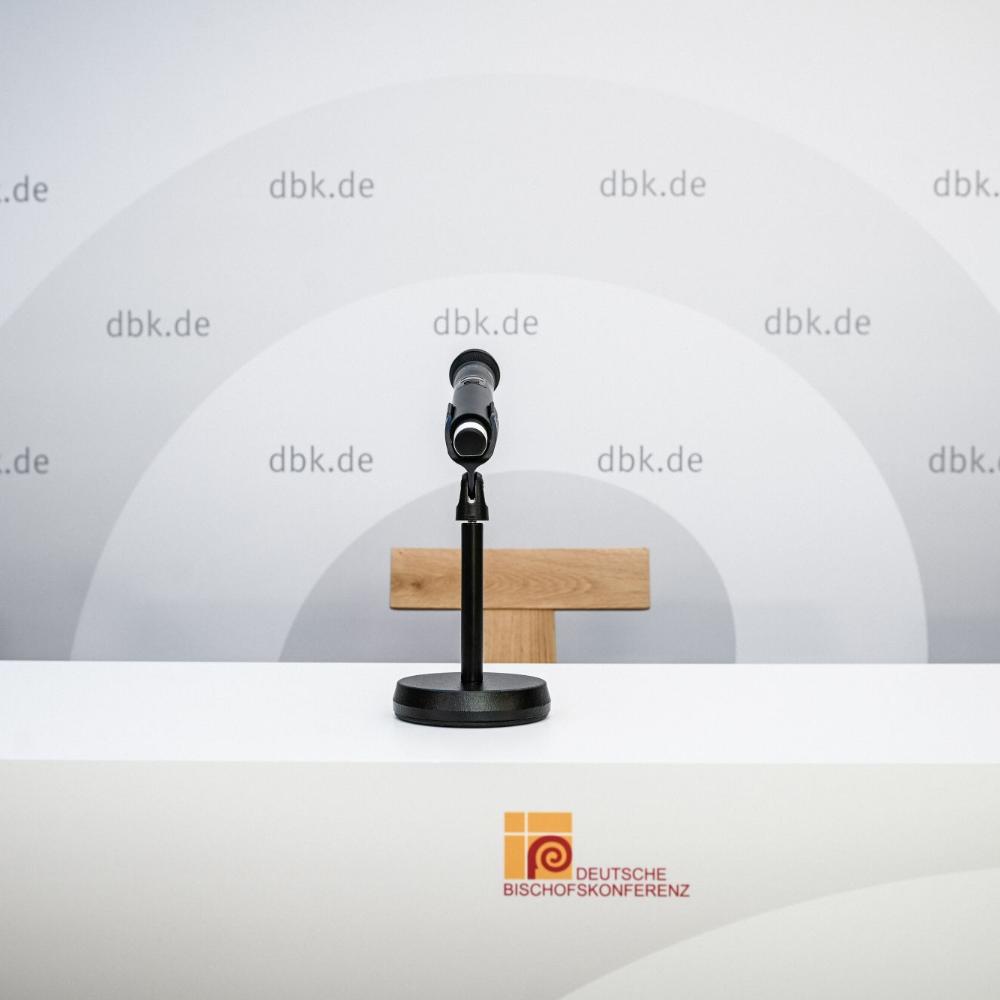 Ein Mikrofon vor einem leeren Stuhl, hinten eine Wand mit DBK-Logo
