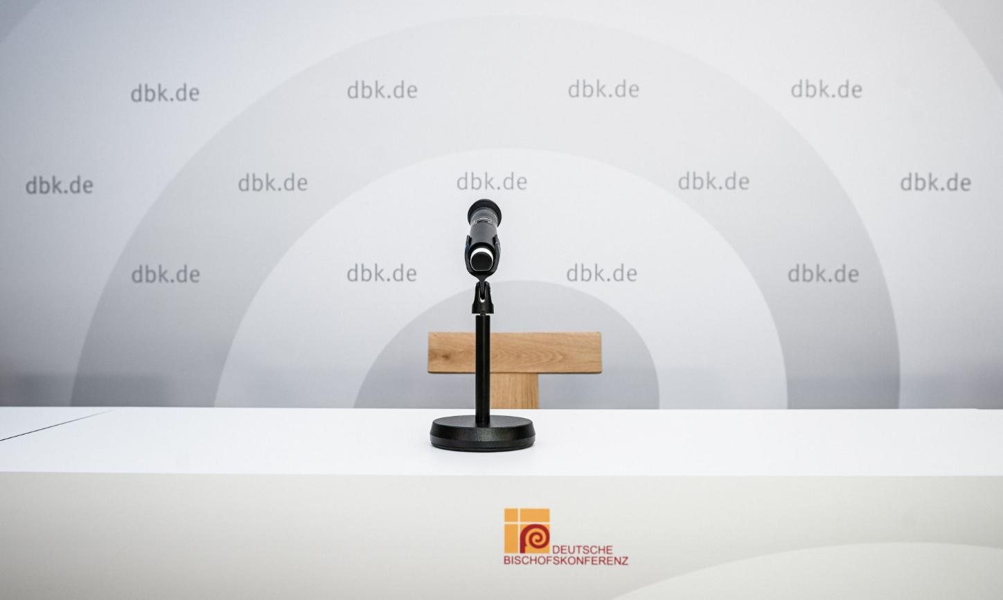Ein Mikrofon vor einem leeren Stuhl, hinten eine Wand mit DBK-Logo