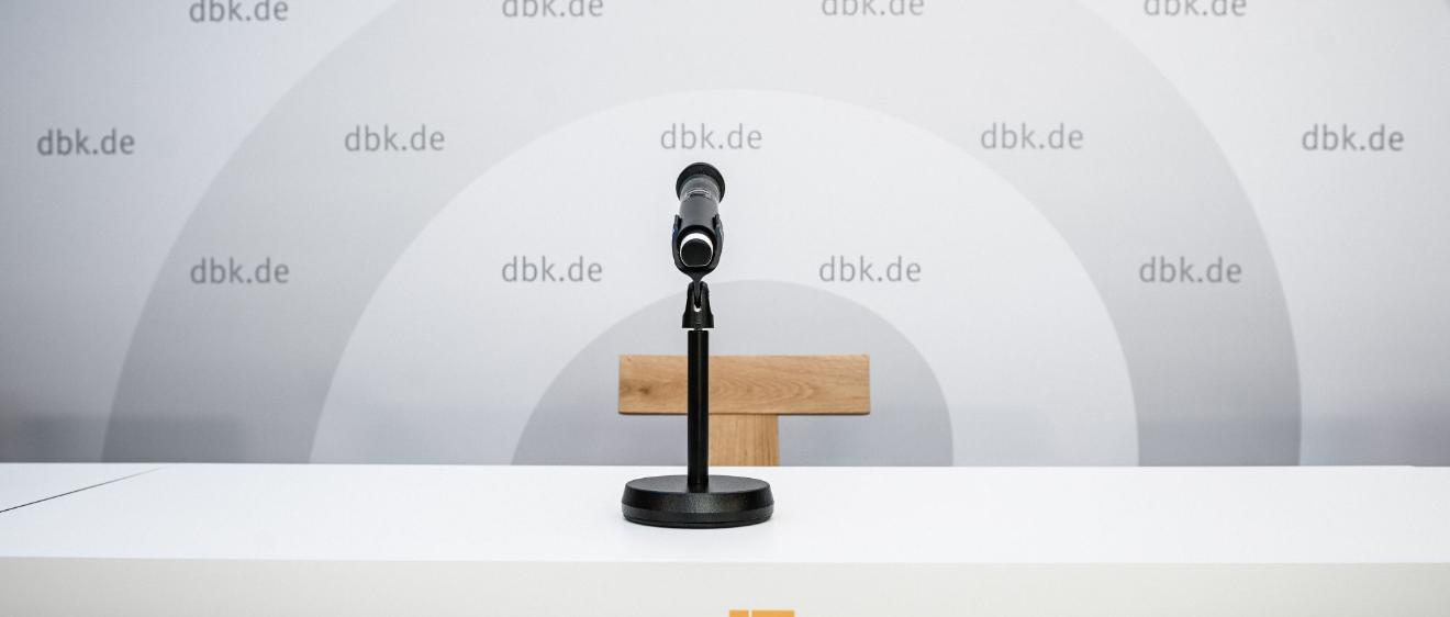 Ein Mikrofon vor einem leeren Stuhl, hinten eine Wand mit DBK-Logo