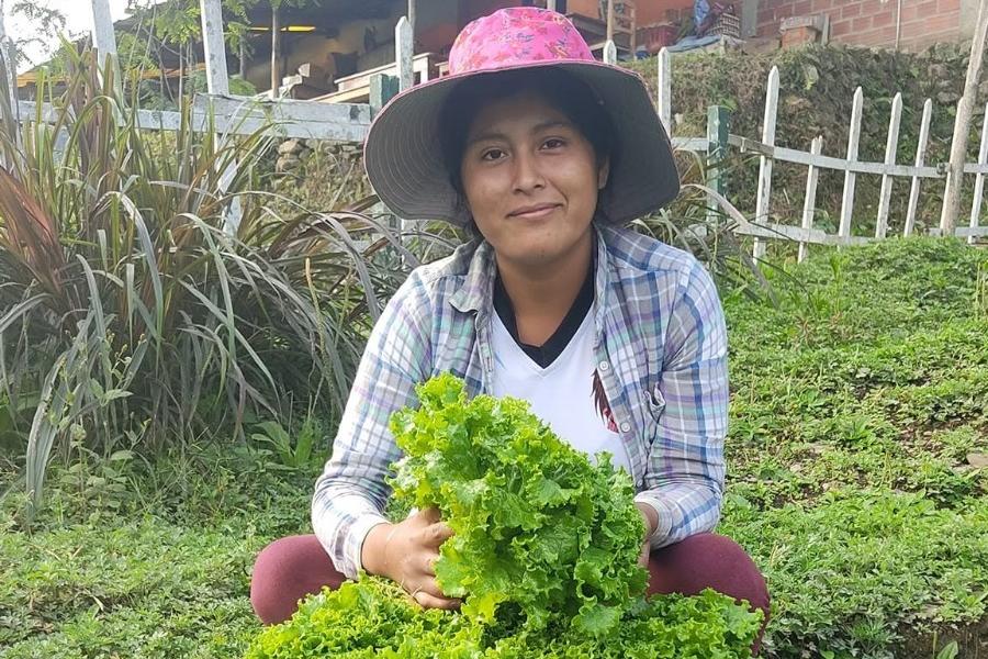 Eine Frau mit Hut lächelt in die Kamera, vor ihr ein Korb mit Salat