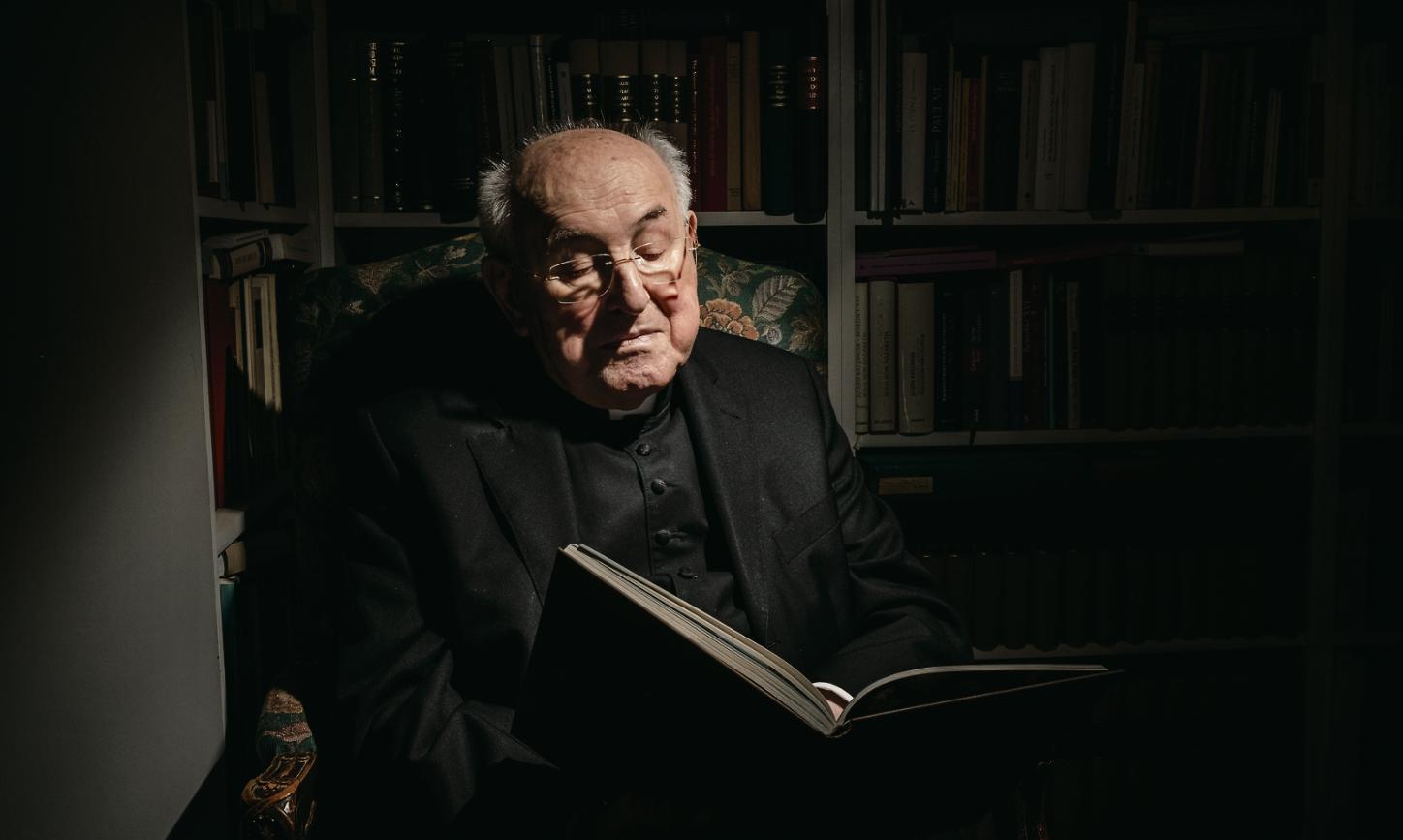 Kardinal Walter Brandmüller sitzt im Sessel und liest in einem Buch.