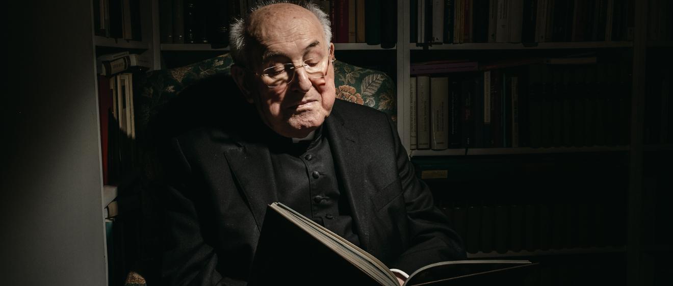 Kardinal Walter Brandmüller sitzt im Sessel und liest in einem Buch.