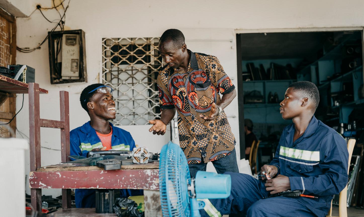 Drei Männer mit dunkler Hautfarbe sitzen an einem Tisch und reparieren etwas
