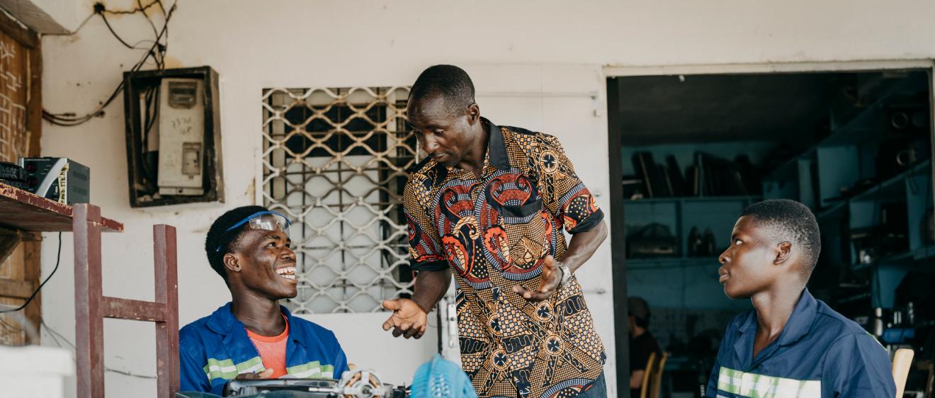 Drei Männer mit dunkler Hautfarbe sitzen an einem Tisch und reparieren etwas
