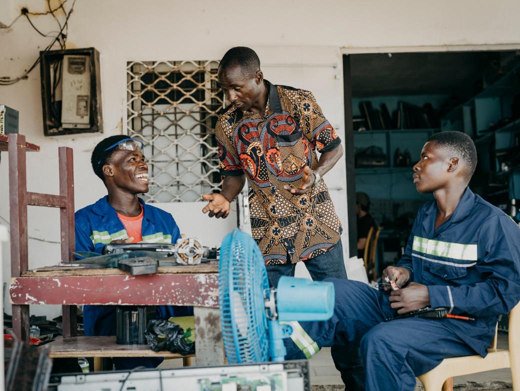 Drei Männer mit dunkler Hautfarbe sitzen an einem Tisch und reparieren etwas