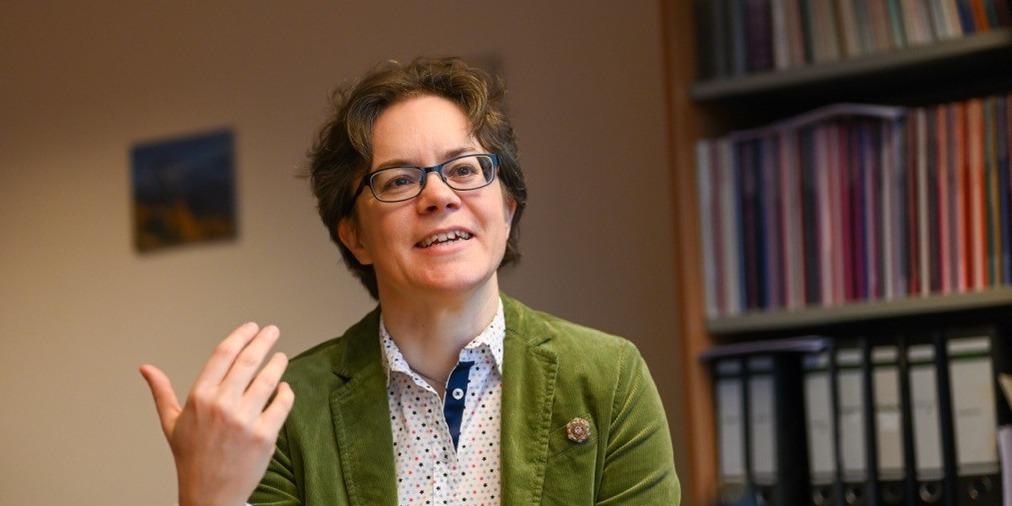 Eine Frau im grünen Blazer hält ein Buch in der Hand und spricht