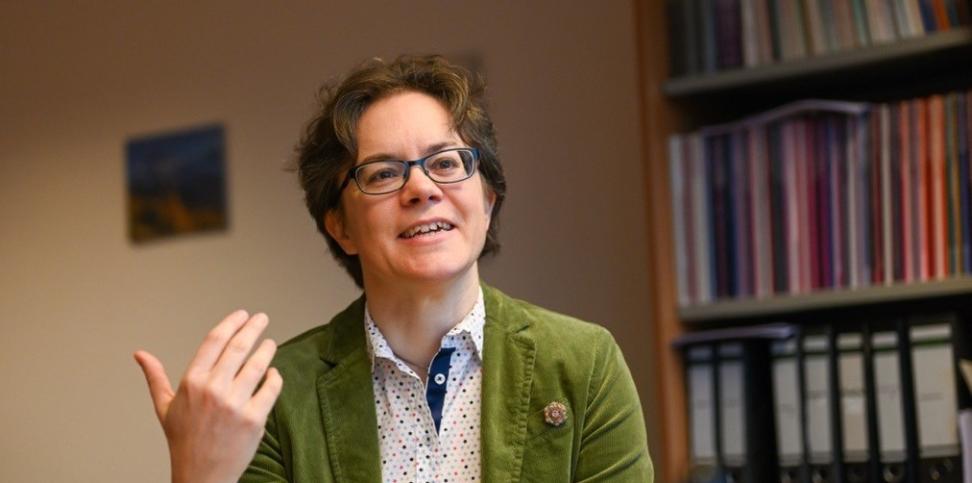 Eine Frau im grünen Blazer hält ein Buch in der Hand und spricht