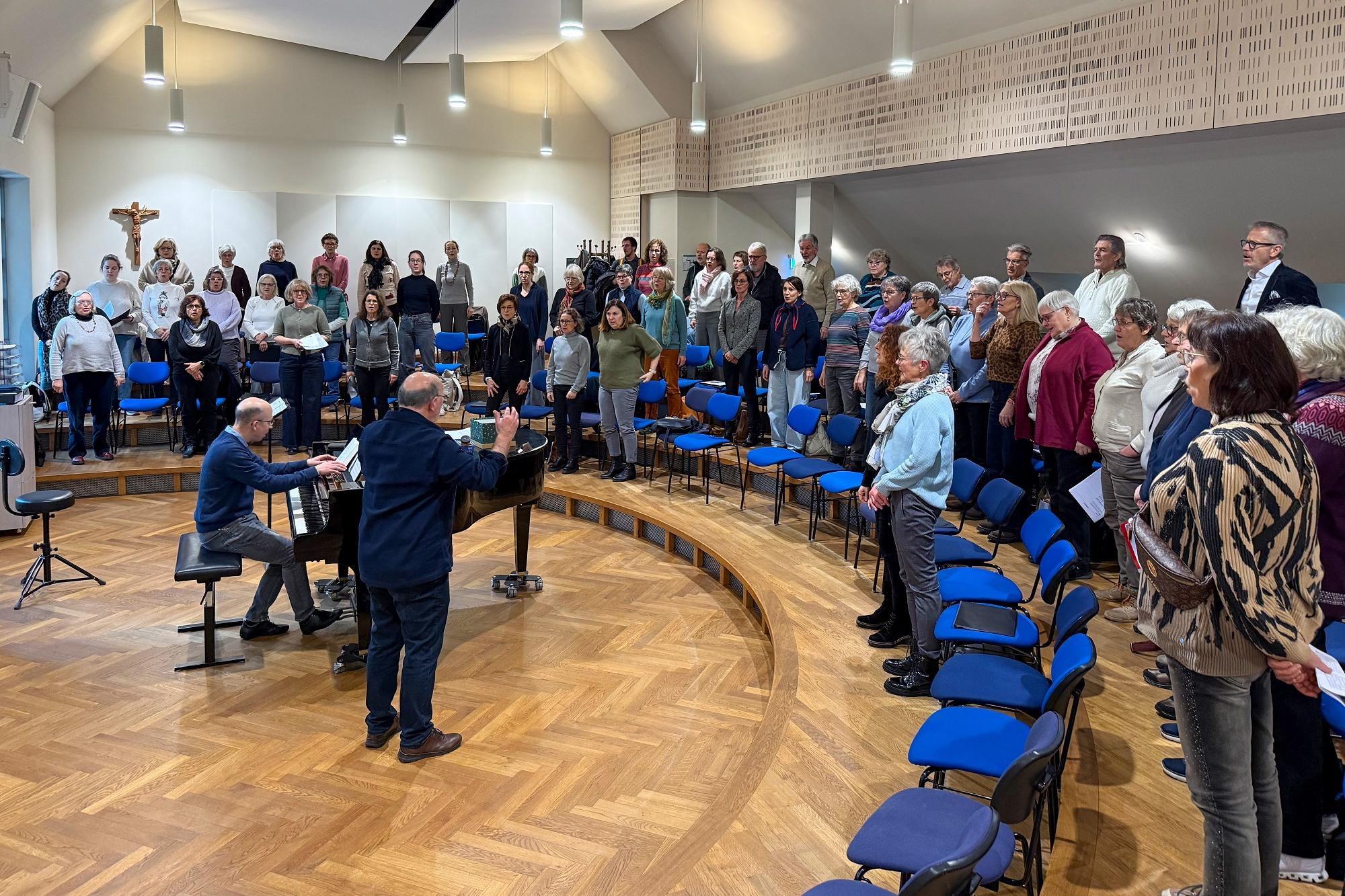 Ein Chor steht im Halbkreis um Dirigent und Pianist.