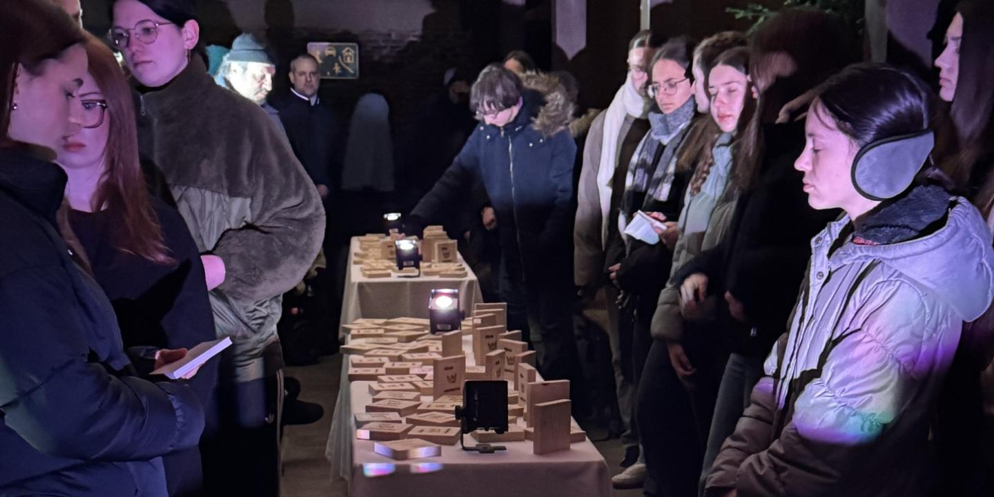 Teilnehmer der Gedenkveranstaltung stehen um Tische mit Holztäfelchenzum Gedenken an jeden der Deportierten.