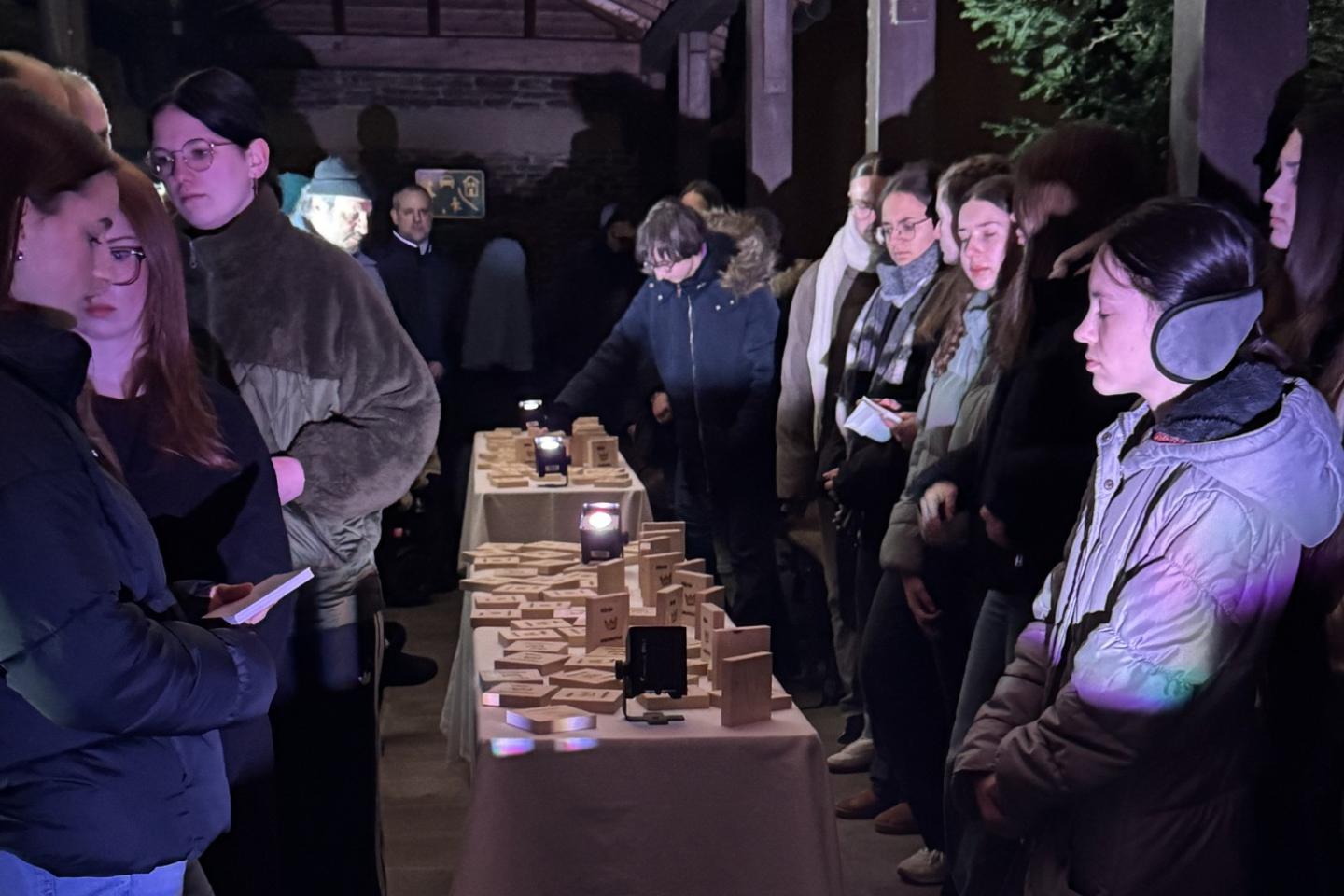 Teilnehmer der Gedenkveranstaltung stehen um Tische mit Holztäfelchenzum Gedenken an jeden der Deportierten.