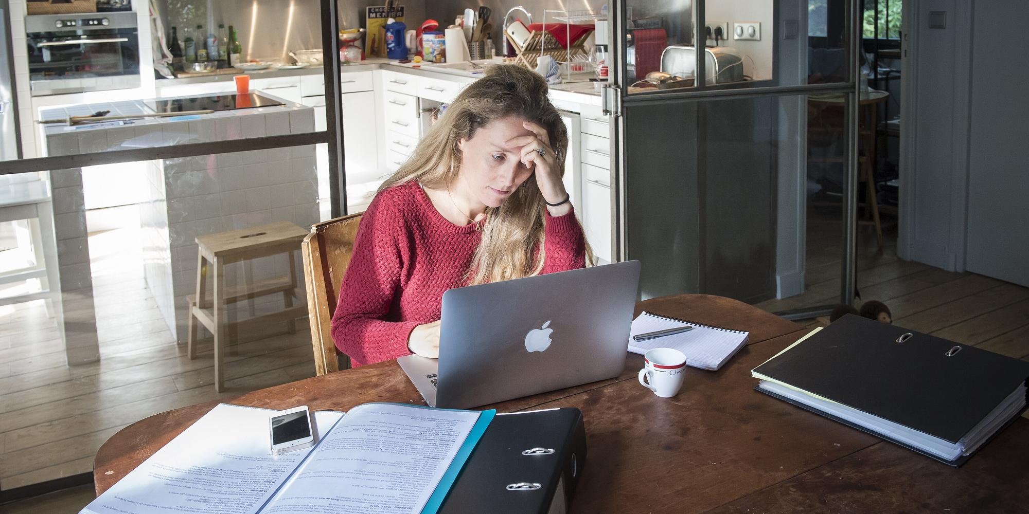 Gestresste Frau mit Aktenordnern und Computer am Schreibtisch.