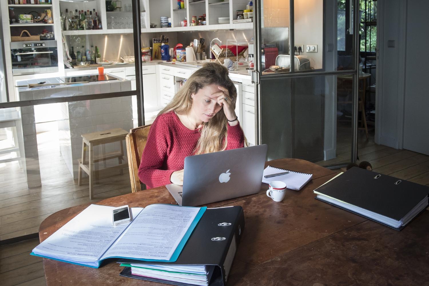 Gestresste Frau mit Aktenordnern und Computer am Schreibtisch.