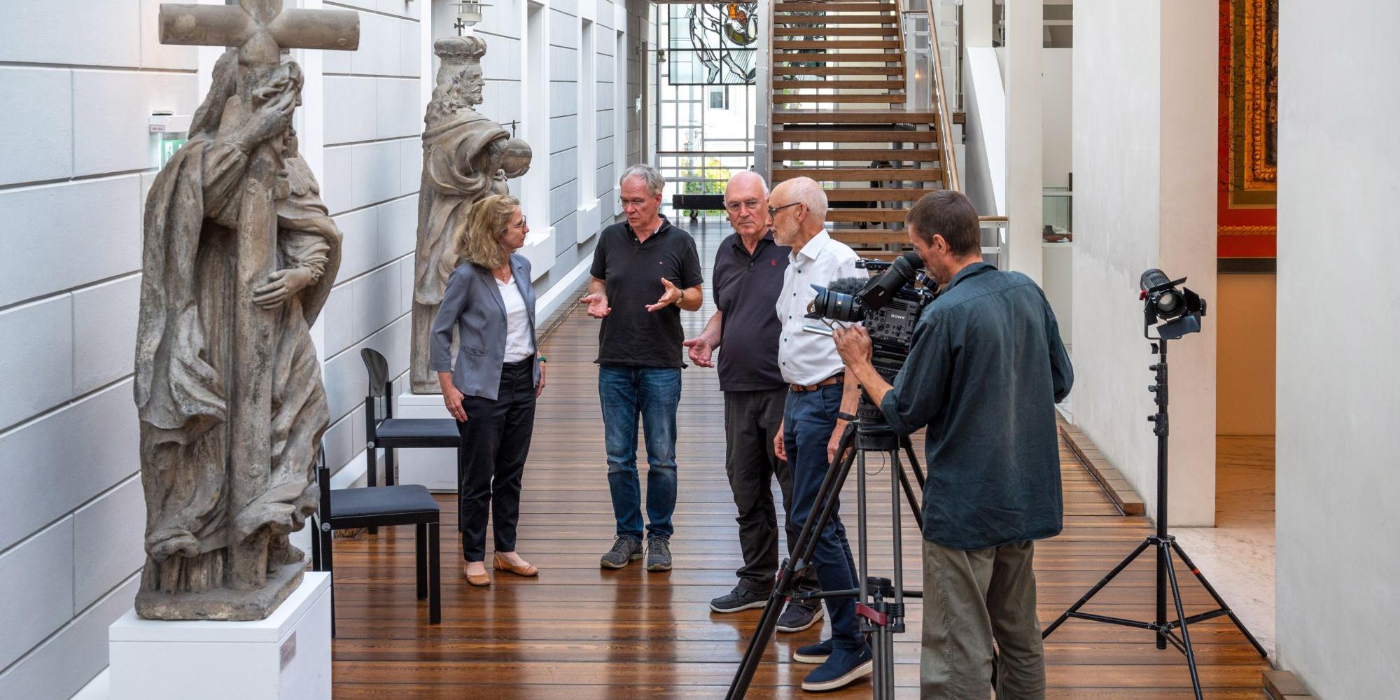 Ein Mann filmt mit einer Kamera, vier Personen im Hintergrund unterhalten sich (c) Rolf Lorig Ein Mann filmt mit einer Kamera, vier Personen im Hintergrund unterhalten sich
