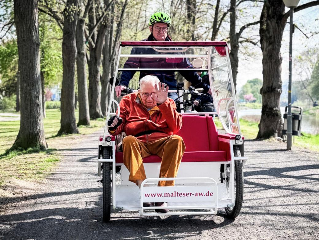 Kurt Braunisch, ehrenamtlicher Mitarbeiter beim Malteser Hilfsdienst, fährt Senior Franz Lieder an der Ahr entlang mit der E-Rikscha in Bad Neuenahr-Ahrweiler.