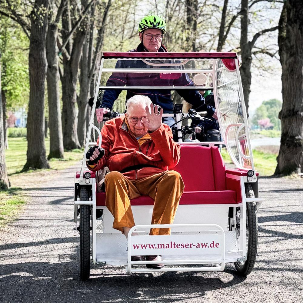 Kurt Braunisch, ehrenamtlicher Mitarbeiter beim Malteser Hilfsdienst, fährt Senior Franz Lieder an der Ahr entlang mit der E-Rikscha in Bad Neuenahr-Ahrweiler.