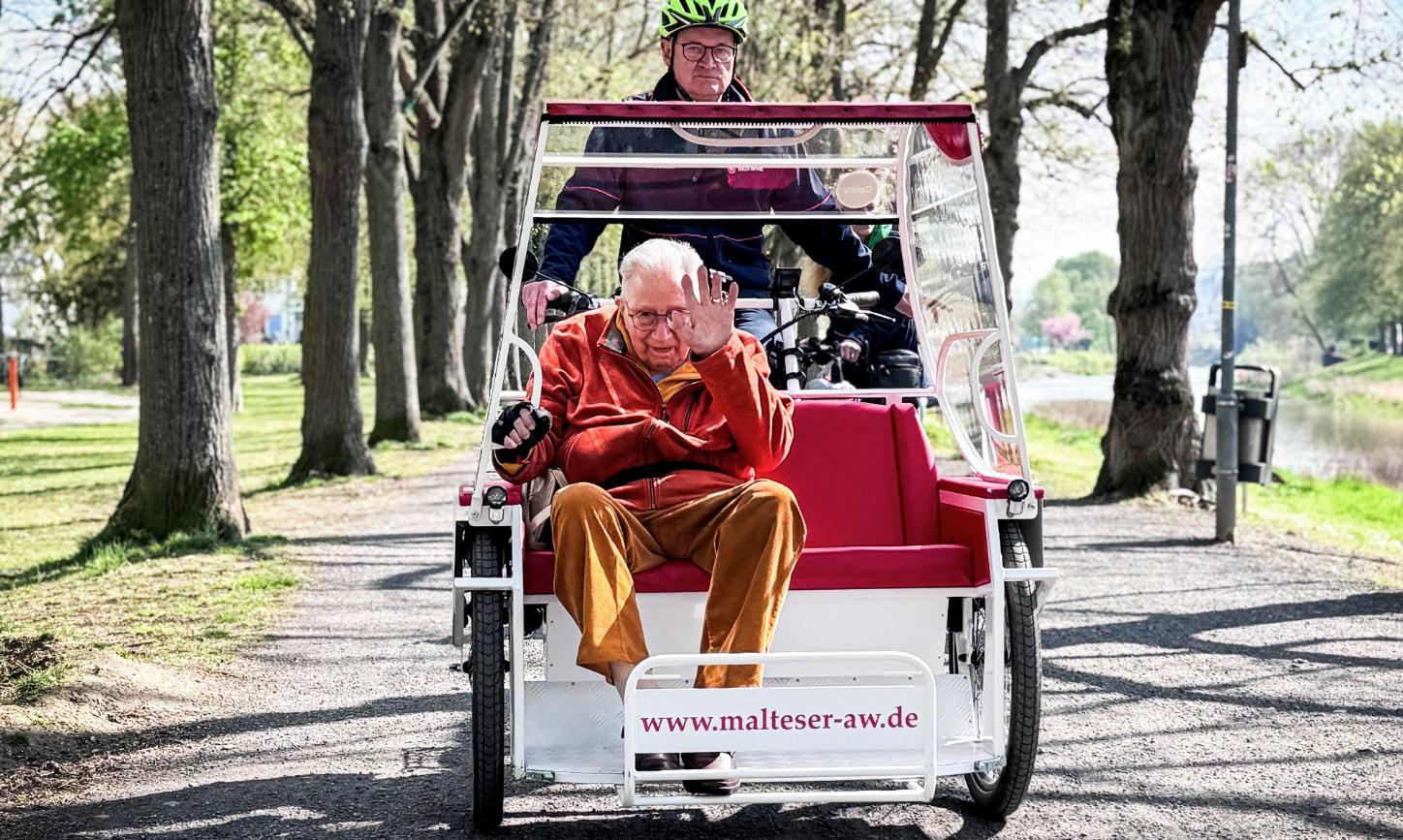 Kurt Braunisch, ehrenamtlicher Mitarbeiter beim Malteser Hilfsdienst, fährt Senior Franz Lieder an der Ahr entlang mit der E-Rikscha in Bad Neuenahr-Ahrweiler.