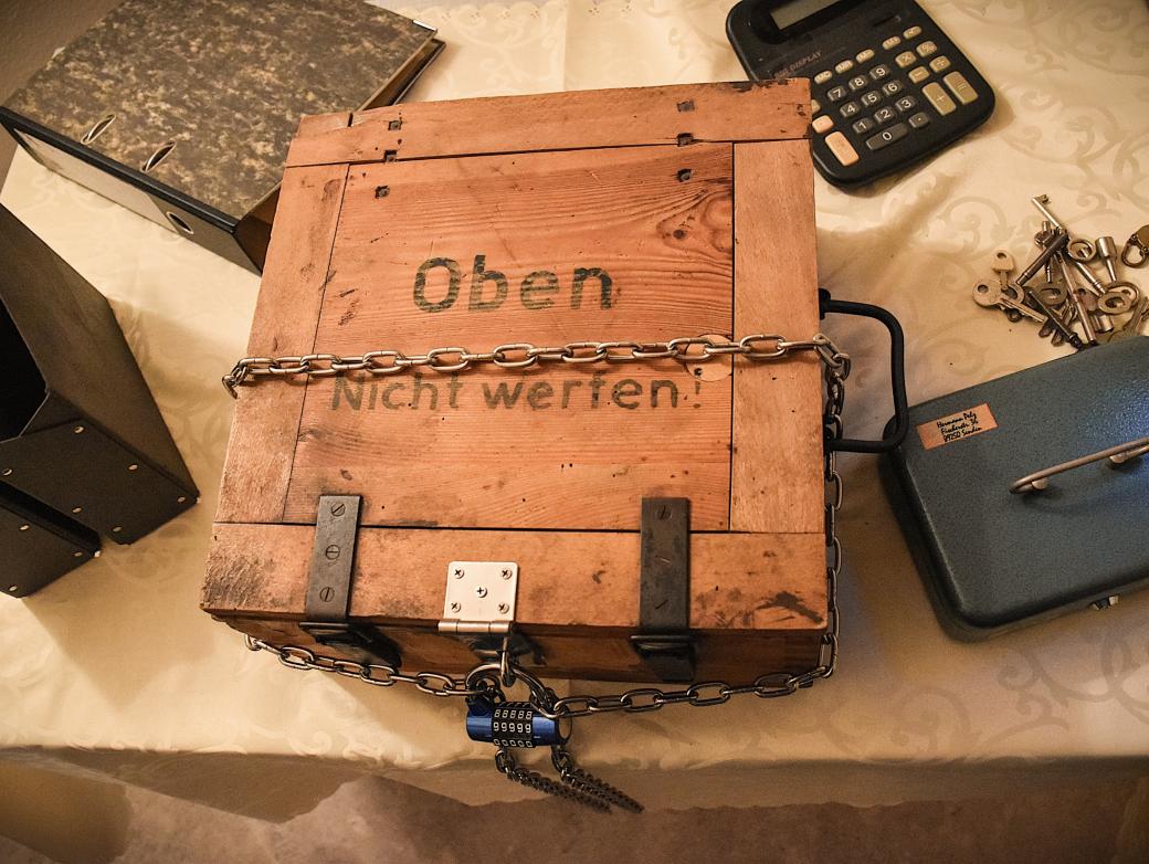 Kiste, Ordner, Taschenrechner, Schlüssel und Kasse verteilt auf einem Tisch sind Bestandteile des Rätsels.