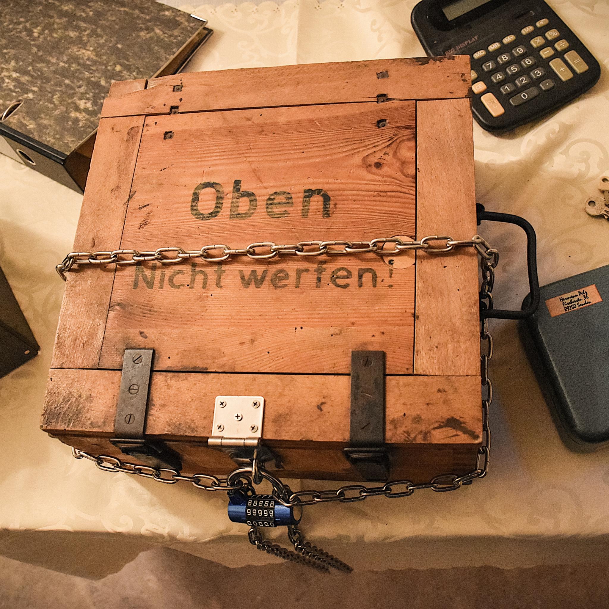 Kiste, Ordner, Taschenrechner, Schlüssel und Kasse verteilt auf einem Tisch sind Bestandteile des Rätsels.