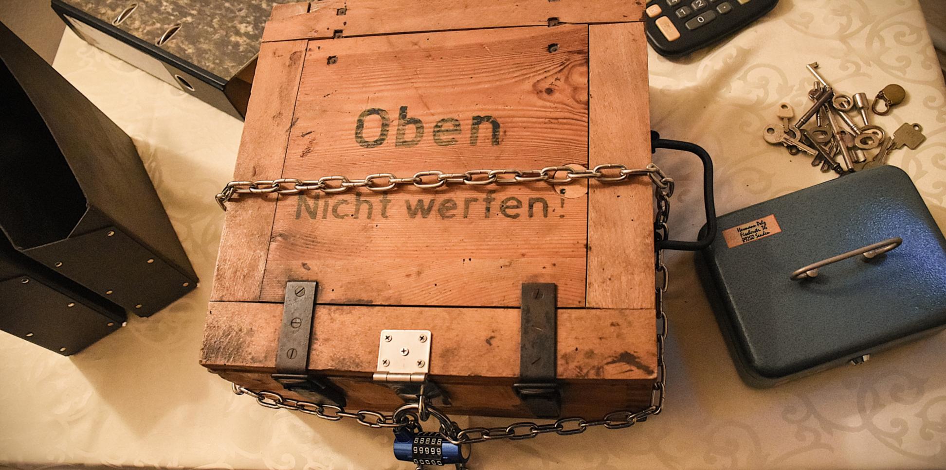 Kiste, Ordner, Taschenrechner, Schlüssel und Kasse verteilt auf einem Tisch sind Bestandteile des Rätsels.