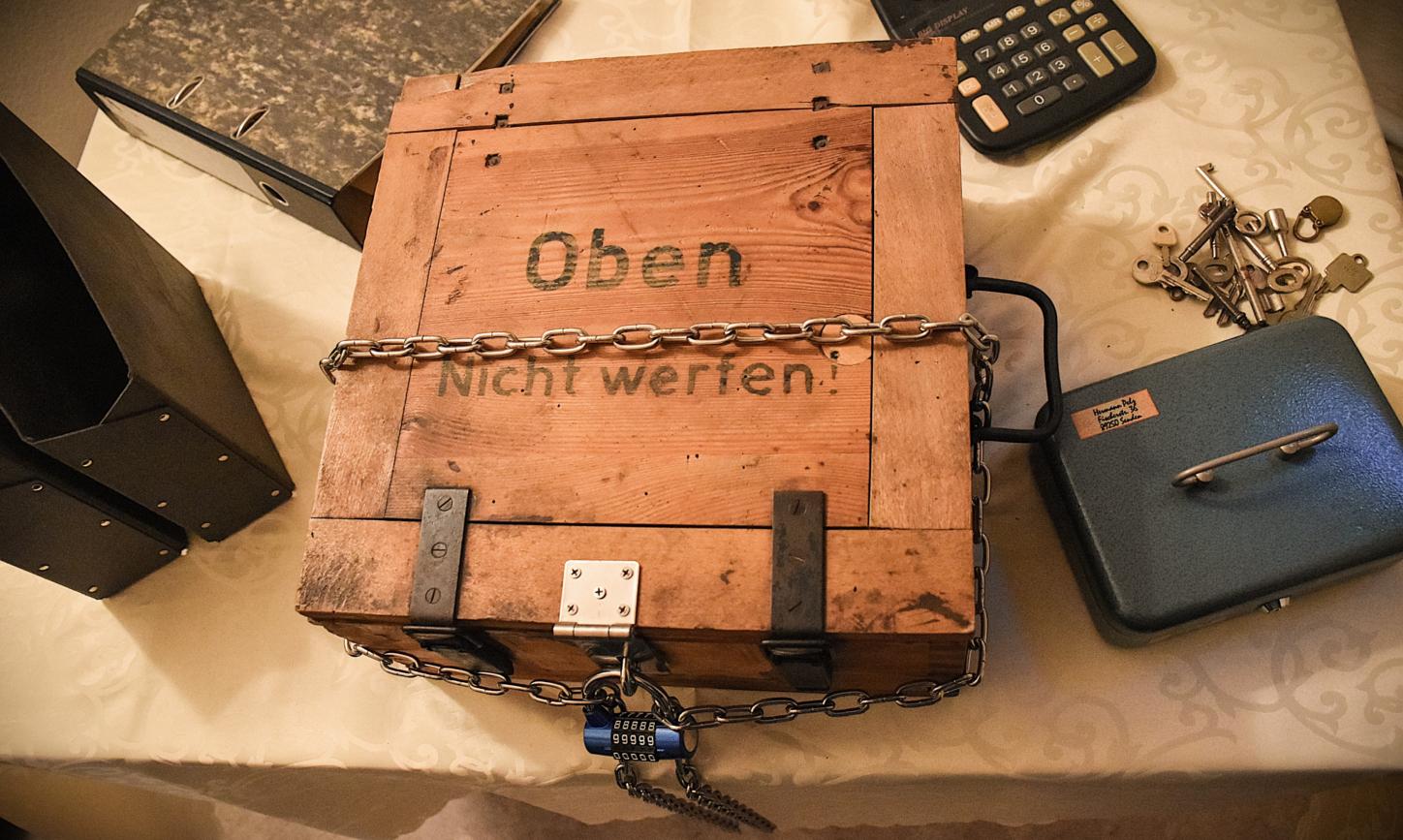 Kiste, Ordner, Taschenrechner, Schlüssel und Kasse verteilt auf einem Tisch sind Bestandteile des Rätsels.