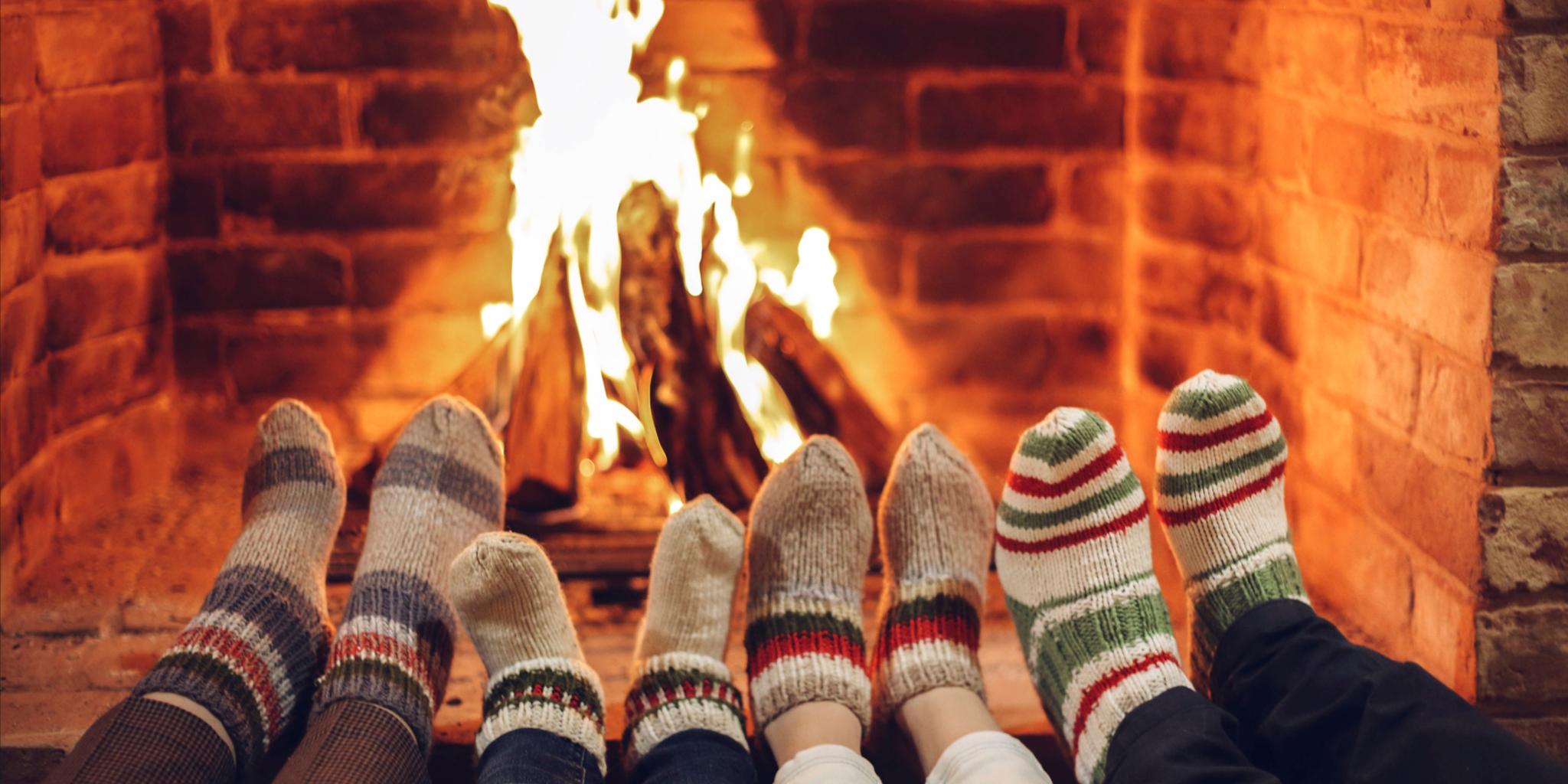 Vier paar Füße in dicken Socken werden an ein offenes Kaminfeuer gestreckt.