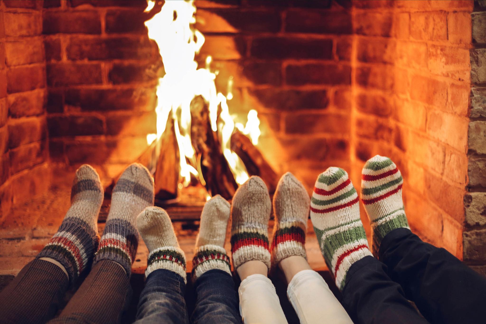 Vier paar Füße in dicken Socken werden an ein offenes Kaminfeuer gestreckt.