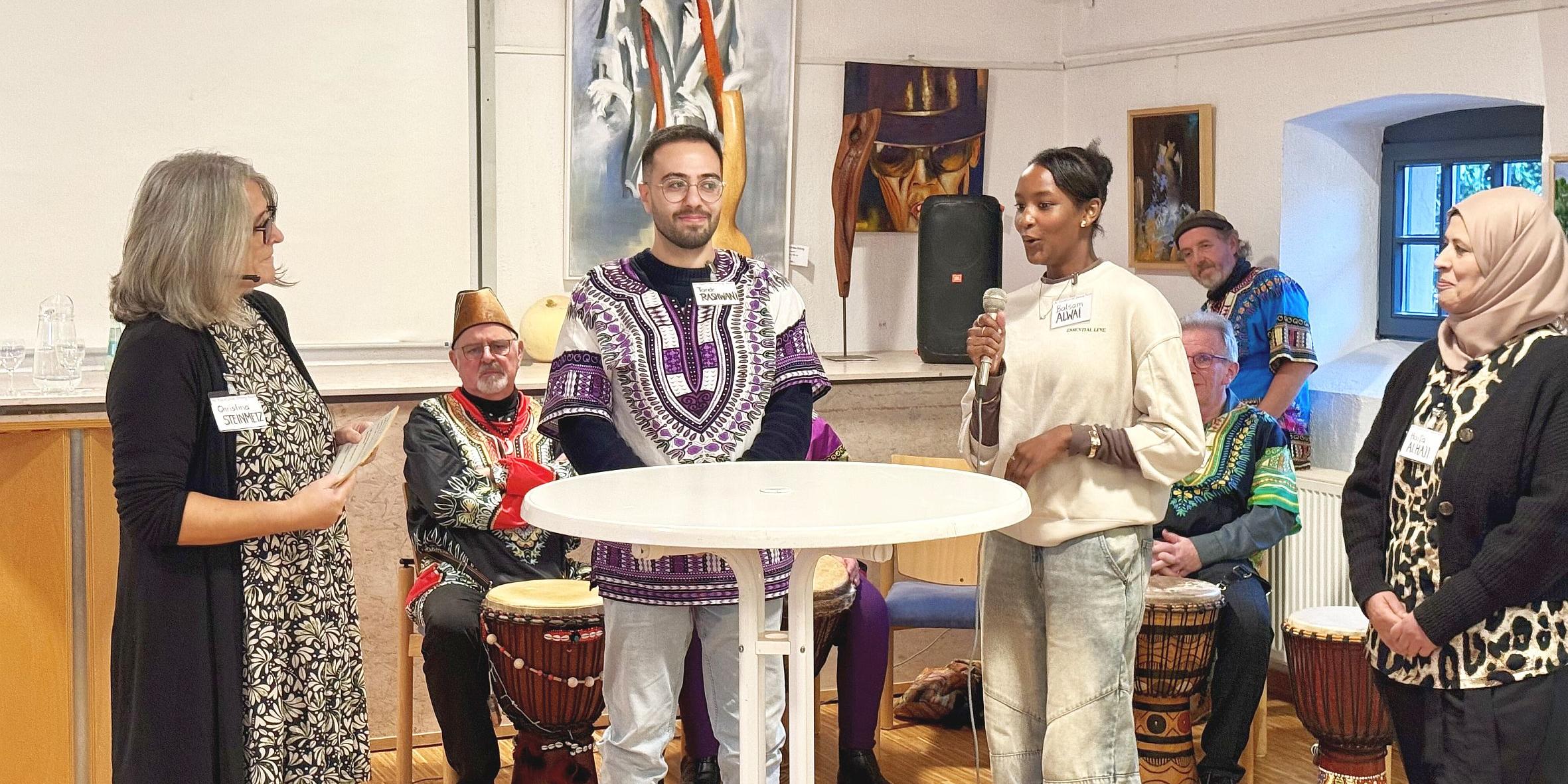 Vier Personen an einem Stehtisch, eine davon spricht in ein Mikrofon. Im Hintergrund sitzen Trommler in Tracht. (c) Kathrin Schmitt Vier Personen an einem Stehtisch, eine davon spricht in ein Mikrofon. Im Hintergrund sitzen Trommler in Tracht.