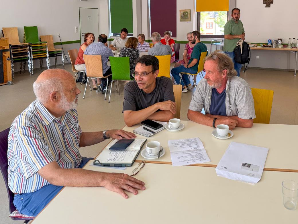 Drei Männer sitzen an einem Tisch, vor ihnen liegen Papiere