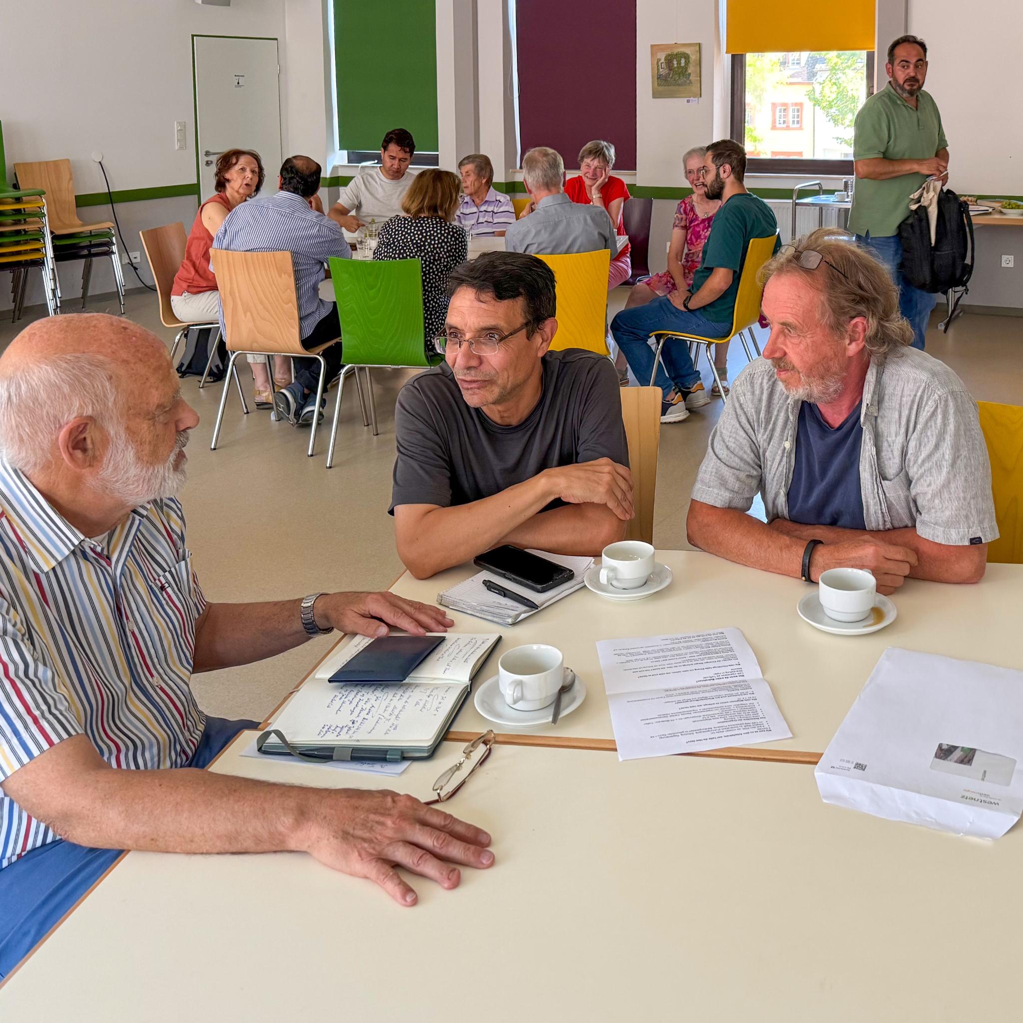 Drei Männer sitzen an einem Tisch, vor ihnen liegen Papiere