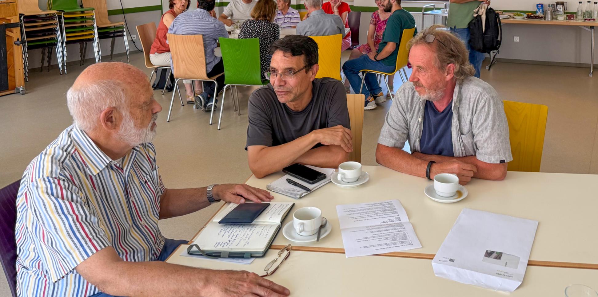 Drei Männer sitzen an einem Tisch, vor ihnen liegen Papiere