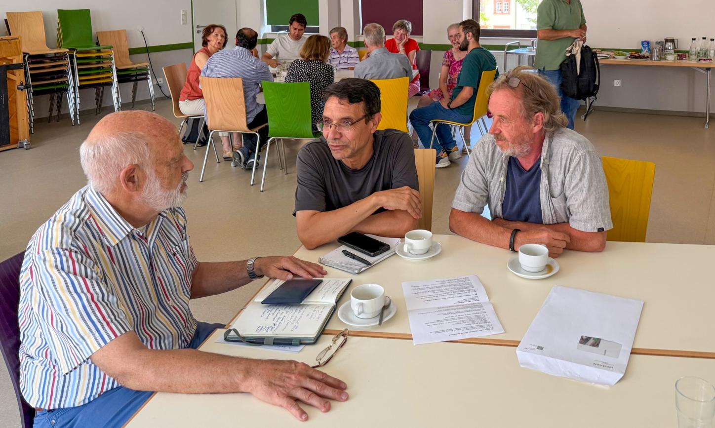 Drei Männer sitzen an einem Tisch, vor ihnen liegen Papiere