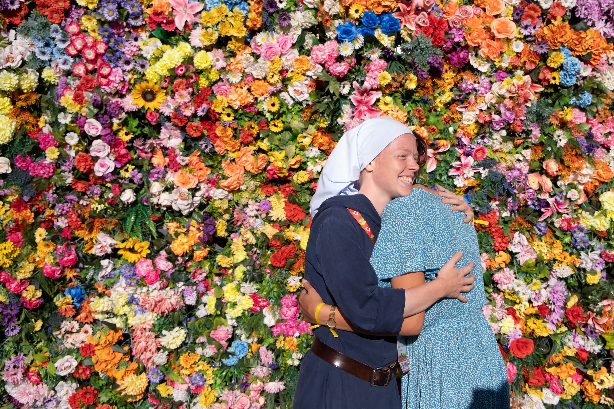 Zwei Frauen umarmen sich vor einer Wand aus Blumen.