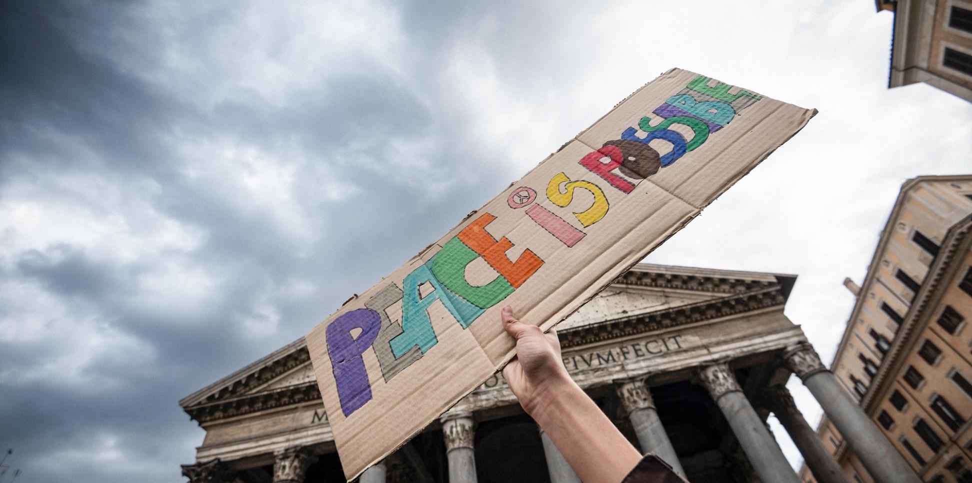 Ein Stück Pappe mit der Aufschrift „Peace is possible“ – „Frieden ist möglich“ wird hochgehalten.