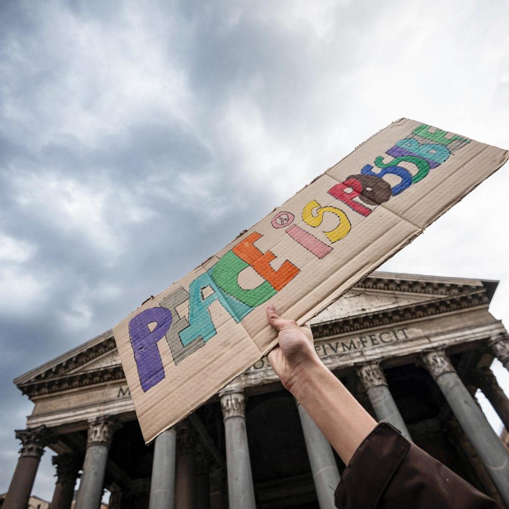 Ein Stück Pappe mit der Aufschrift „Peace is possible“ – „Frieden ist möglich“ wird hochgehalten.