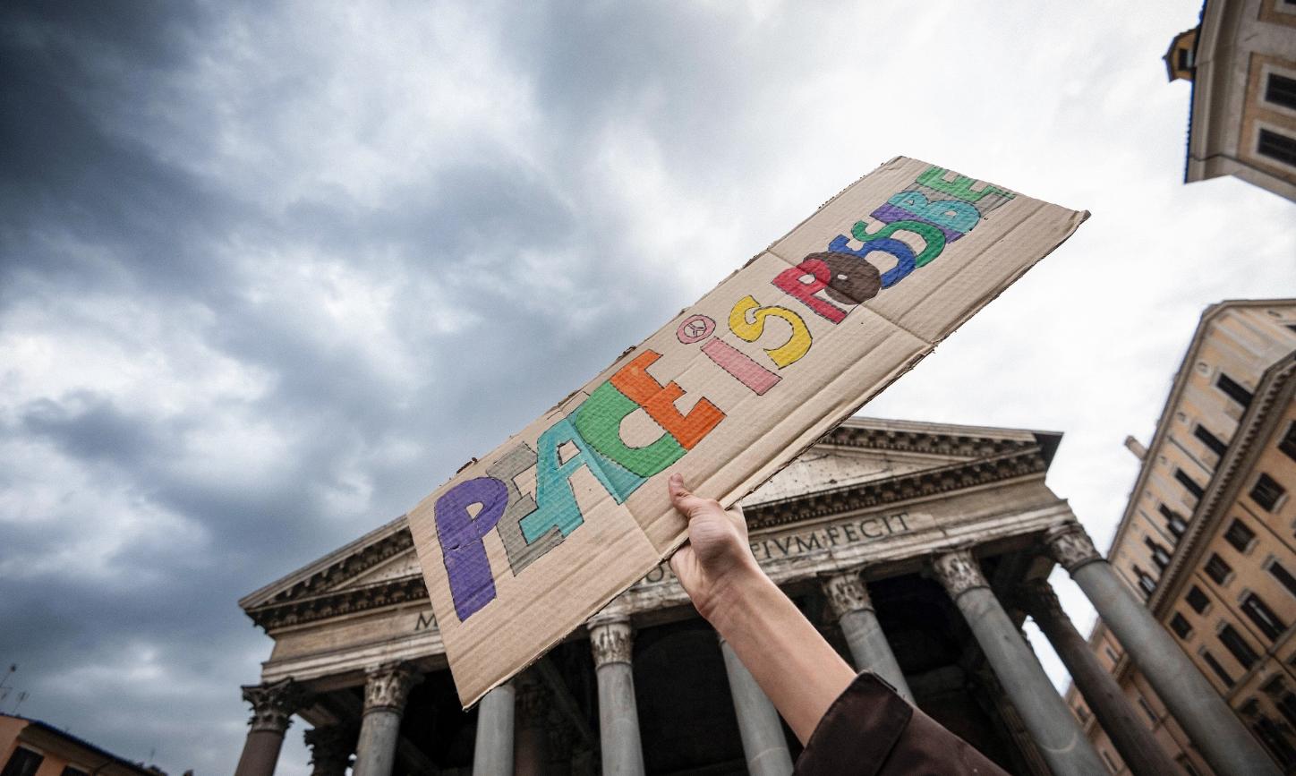 Ein Stück Pappe mit der Aufschrift „Peace is possible“ – „Frieden ist möglich“ wird hochgehalten.