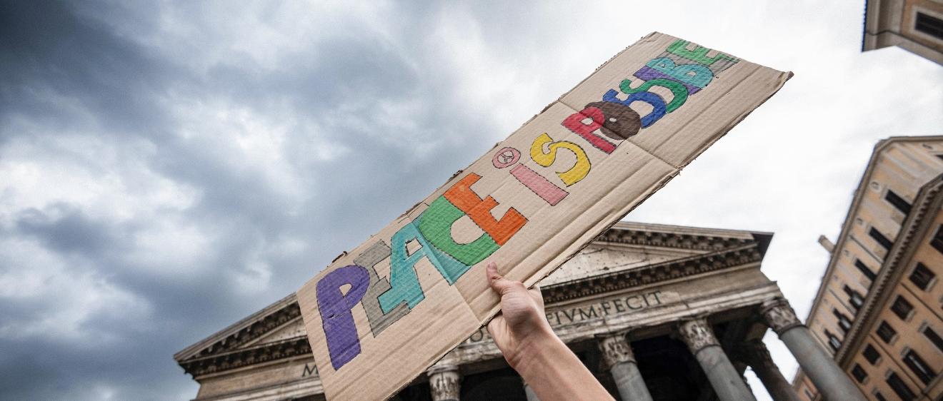 Ein Stück Pappe mit der Aufschrift „Peace is possible“ – „Frieden ist möglich“ wird hochgehalten.