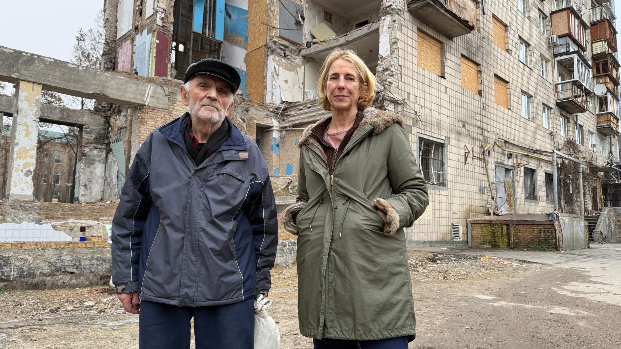 Ein Frau und ein Mann stehen vor einem zerbombten Haus.
